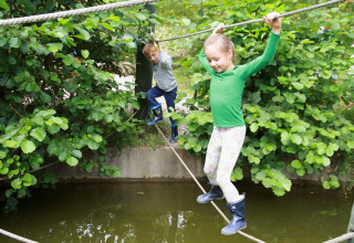 Twee kinderen balanceren op een touw boven water bij Familiepark Sottrum, Boomhutten glamping in Nedersaksen.