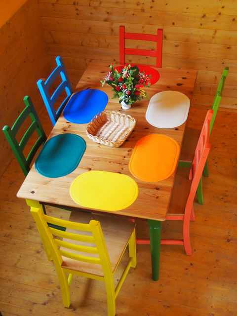 Table à manger colorée avec six chaises différentes et sets dans un chalet en bois à Familiepark Sottrum.