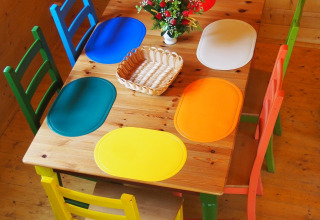 Kleurrijke eettafel met zes verschillende stoelen en placemats in een houten hut bij Familiepark Sottrum.