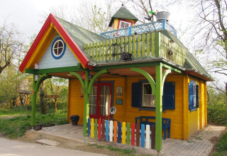 Cabane en bois colorée de glamping à Familiepark Sottrum, avec balcon, clôture et entourée de verdure.