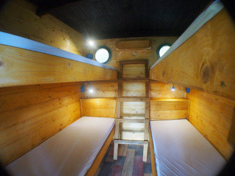 Four beds in a cozy wooden treehouse room with round windows and reading lights, Familiepark Sottrum.