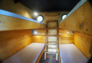 Quattro letti in una stanza di casetta sull'albero in legno con finestre rotonde e luci da lettura.