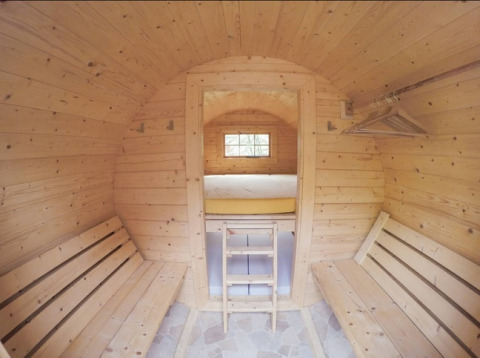 Interieur van een houten hut met banken, bed en kledingrek, Familiepark Sottrum Boomhutten Nedersaksen.