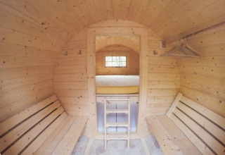 Innenansicht einer Holzhütte mit Bänken, Bett und Kleiderstange, Familiepark Sottrum Boomhutten.