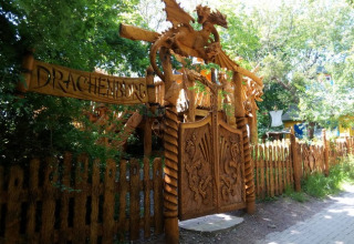 Entree van Familiepark Sottrum - Boomhutten Nedersaksen met houten poort en draak, omgeven door groen.