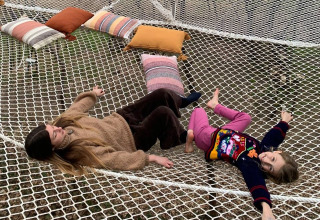 Madre e hija relajándose en una gran red con cojines en Azienda Agricola Il Granello Glampingtent Italia.