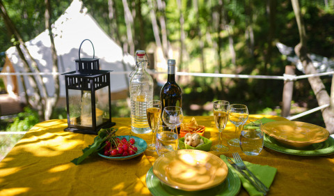 Tavolo all'aperto con vino, snack e lanterna vicino alla tenda glamping Azienda Agricola Il Granello in Italia.