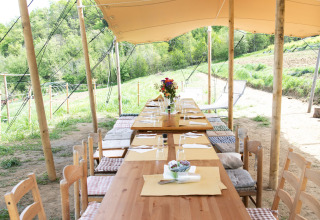 Buiten eetgedeelte met houten tafels onder een tent bij Azienda Agricola Il Granello Glampingtent Italië.