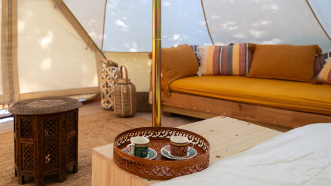 Interior de tienda glamping en Italia con muebles de madera, cojines coloridos y bandeja de té en la mesa.