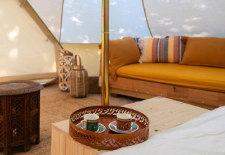 Interno di una tenda glamping di lusso in Italia con cuscini colorati, mobili in legno e vassoio da tè.
