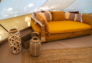 Cozy glamping tent accommodation at Azienda Agricola Il Granello with yellow sofa and woven decor.