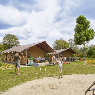Gezin geniet buiten voor glampingtenten bij Recreatiepark TerSpegelt LoungeLodge Glamping, Noord-Brabant.