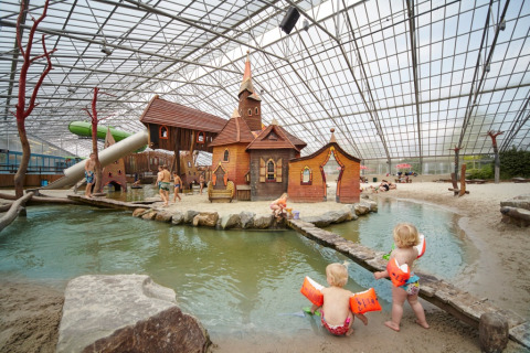 Children playing at an indoor water park featuring sandy beaches and whimsical huts at LoungeLodge Glamping Noord-Brabant.
