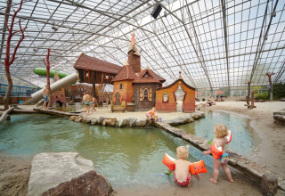 Children playing at an indoor water park featuring sandy beaches and whimsical huts at LoungeLodge Glamping Noord-Brabant.