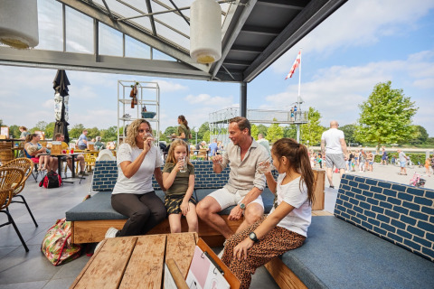 Familia disfruta bebidas al aire libre en LoungeLodge Glamping de Recreatiepark TerSpegelt en Noord-Brabant.