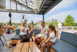 Family relaxing with drinks at the LoungeLodge Glamping in Recreatiepark TerSpegelt, Noord-Brabant, outdoors.