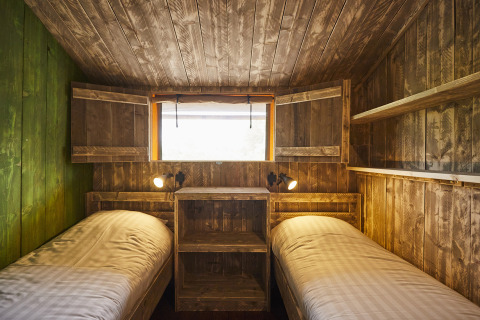 Hébergement glamping LoungeLodge confortable avec deux lits simples, murs en bois rustique et fenêtre.