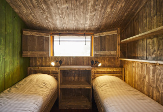 Gezellige LoungeLodge Glamping accommodatie met twee eenpersoonsbedden, houten muren en een raam.