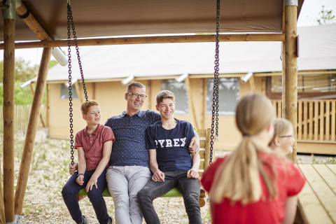 Family sits together on an outdoor swing during a glamping vacation at LoungeLodge, Recreatiepark TerSpegelt, Noord-Brabant.