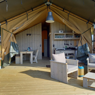 Tienda tipo safari de glamping de lujo con terraza de madera, muebles modernos y zona exterior en Holanda.
