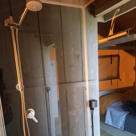 Innenansicht eines Glamping-Safari-Zeltes in Heemskerkerduin mit Dusche und Schlafbereich in Nordholland.