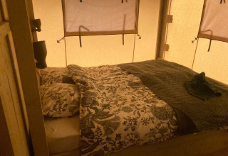 Glamping Heemskerkerduin - Safari tent in Noord Holland featuring a cozy double bed in warm yellow lighting.