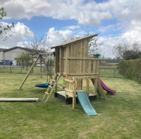 Legeplads med gyngestativ, rutsjebaner og legehus i have ved Glamping Heemskerkerduin, Safaritenten i Noord-Holland.