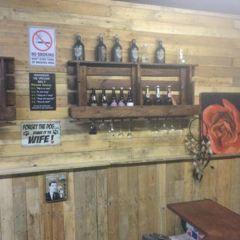 Mur de bar rustique à Glamping Heemskerkerduin avec bouteilles, panneaux, verres et tableau de rose.