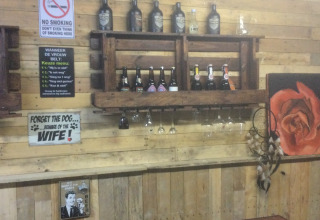 Parete rustica del bar a Glamping Heemskerkerduin con bottiglie di birra, insegne, bicchieri e rosa.