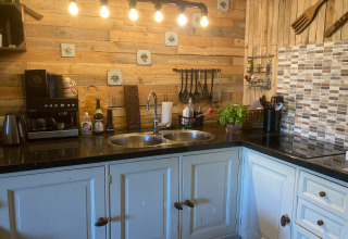 Cuisine glamping chaleureuse à Safaritenten Noord-Holland avec murs en bois, équipements modernes et éclairage doux.