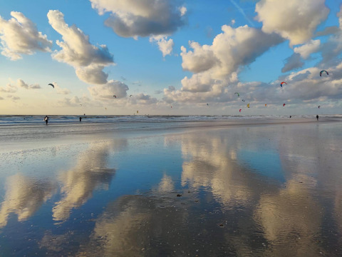 Abendstimmung am Strand mit Spiegelung der Wolken und Kite-Surfern nahe Glamping Heemskerkerduin, Holland.
