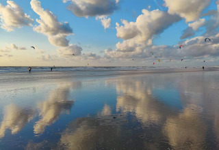 Coucher de soleil sur la plage avec des nuages reflétés et des kite-surfeurs près de Glamping Heemskerkerduin.