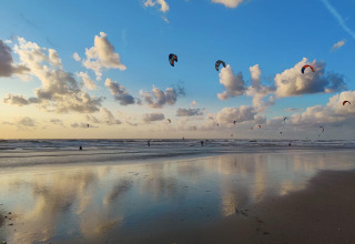 Kitesurfeurs sur la plage de Glamping Heemskerkerduin - Safaritenten Noord-Holland sous un ciel bleu.