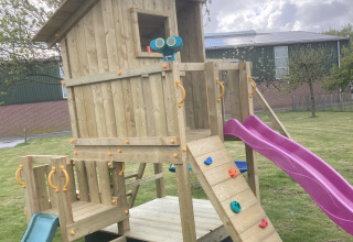 Legeplads med trætårn, klatrevæg, lilla rutsjebane og grøn rutsjebane på Glamping Heemskerkerduin.