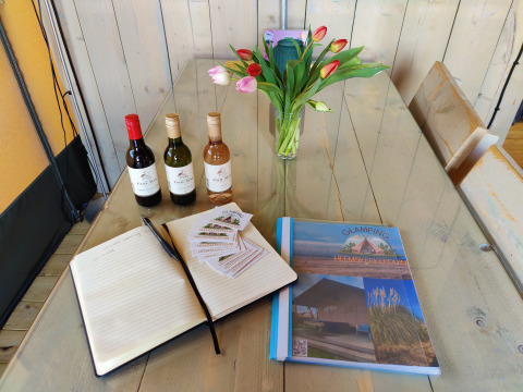 Mesa de glamping con botellas de vino, libro de visitas, folletos, tulipanes y carpeta de Glamping Heemskerkerduin.
