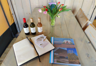 Tavolo glamping con bottiglie di vino, guestbook, brochure, tulipani e cartella Glamping Heemskerkerduin.