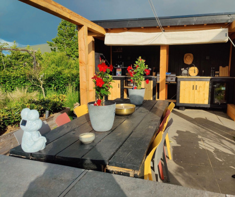Área de comedor al aire libre en Glamping Heemskerkerduin Safaritenten Noord-Holland con flores y cocina.