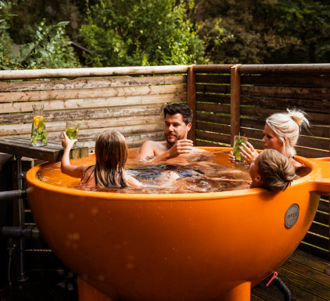 Familia relajándose en una bañera de hidromasaje naranja al aire libre en Buitenplaats Beekhuizen Glamping Veluwe.