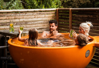 Gezin ontspant in een oranje buitenjacuzzi bij Buitenplaats Beekhuizen - Glamping Veluwe.