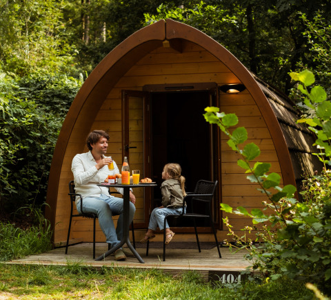 Family enjoying breakfast in front of their wooden cabin at Buitenplaats Beekhuizen Glamping Veluwe.