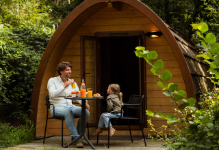 Gezin geniet van ontbijt voor hun houten hutje bij Buitenplaats Beekhuizen Glamping Veluwe in het groen.