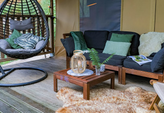 Acogedor salón en tienda glamping de Buitenplaats Beekhuizen Veluwe, con silla colgante y sofá confortable.
