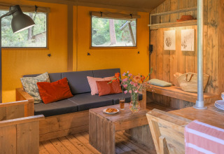 Gezellige glamping accommodatie met bank, houten meubels en bloemen bij Buitenplaats Beekhuizen - Glamping Veluwe.