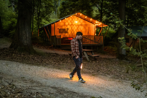 Ein Mann spaziert abends vor einer beleuchteten Hütte bei Buitenplaats Beekhuizen – Glamping Veluwe.
