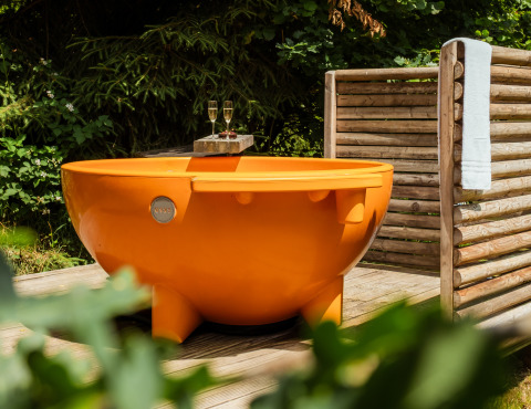 Round outdoor orange bathtub with two wine glasses and towel, glamping at Buitenplaats Beekhuizen Veluwe.
