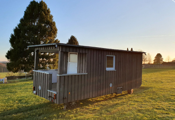 Glamping accommodatie in een houten wagen bij Camping im Bergischen Land, Noordrijn-Westfalen bij zonsopgang.