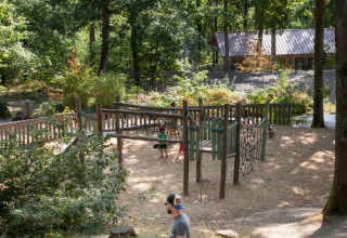 Een gezin wandelt langs een speeltuin in het bos bij Huttopia Wattwiller - Glamping Grand Est.
