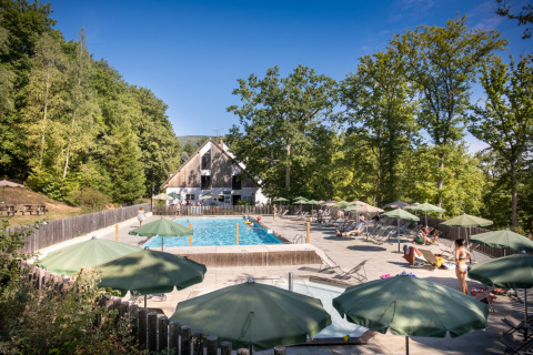 Buitenzwembad met groene parasols en gasten bij Huttopia Wattwiller - Glamping Grand Est.