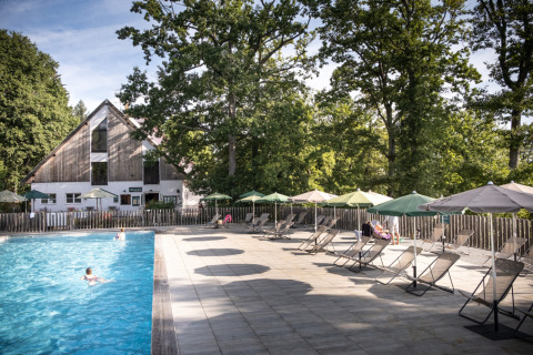 Outdoor swimming pool with deck chairs and umbrellas at Huttopia Wattwiller - Glamping Grand Est location.