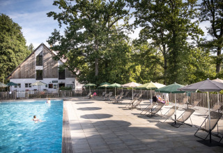 Piscina all'aperto con lettini e ombrelloni presso Huttopia Wattwiller - Glamping Grand Est immerso nel verde.